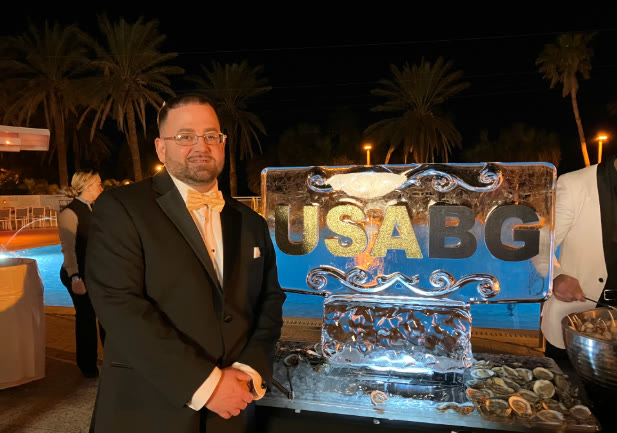 Richard 'Dick' Tracy in a tuxedo at the USA Benefits Group annual gala, beside the USABG ice sculpture